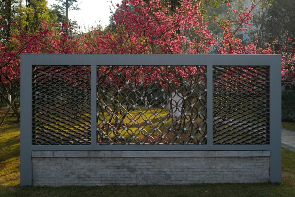 A decorative fence with vibrant flowering trees behind it.