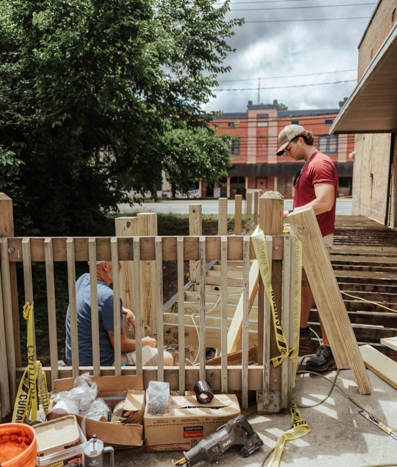 Construction workers build a wooden fence outdoors.